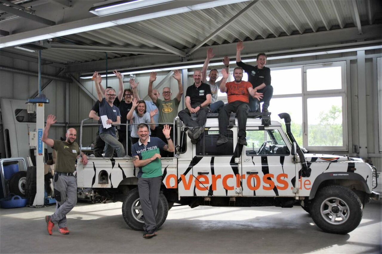 Gruppenfoto der Kursteilnehmer auf einem zebra-gestreiften Land Rover Defender in der Werkstatt