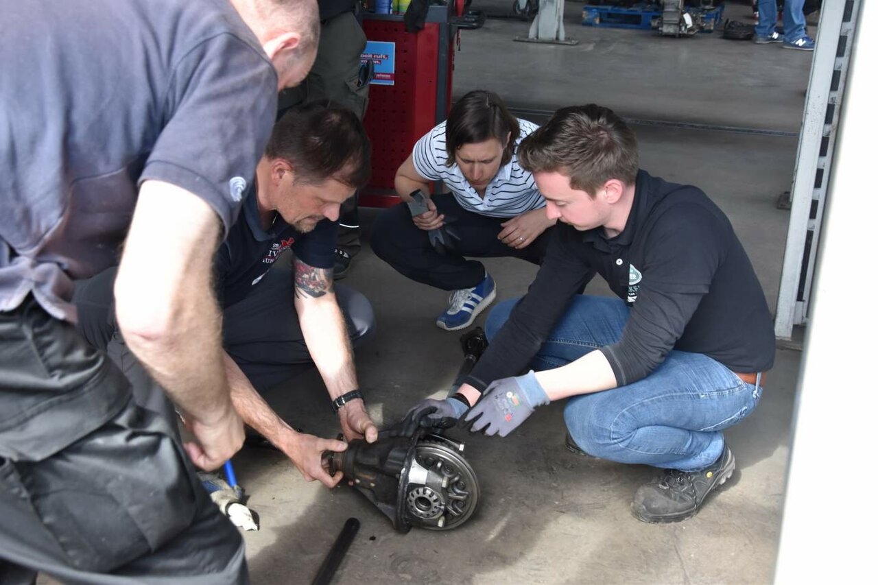 Gruppe kauert um ein ausgebautes Differential auf dem Werkstattboden