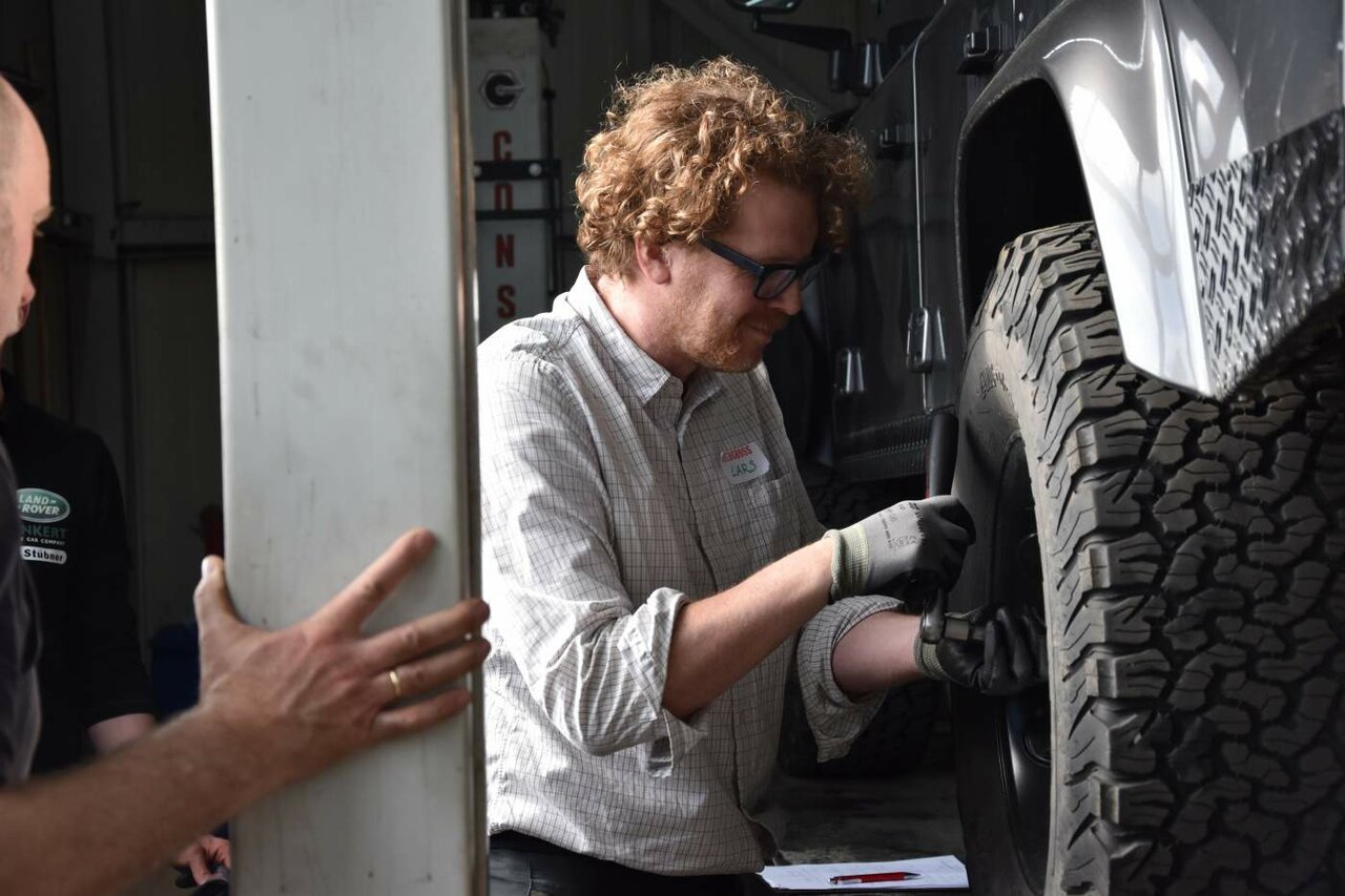 Ein Mechaniker mit Brille dreht mit einem Schraubenschlüssel an der Radnabe eines Geländewagens während des Kurses