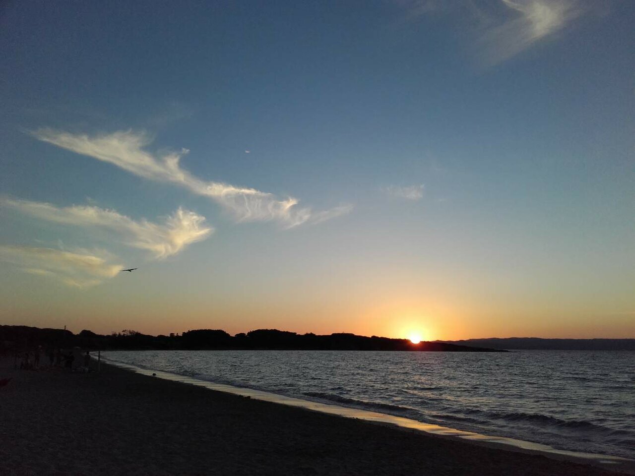 Pôr do sol sobre um mar calmo com um promontório arborizado em silhueta contra o céu
