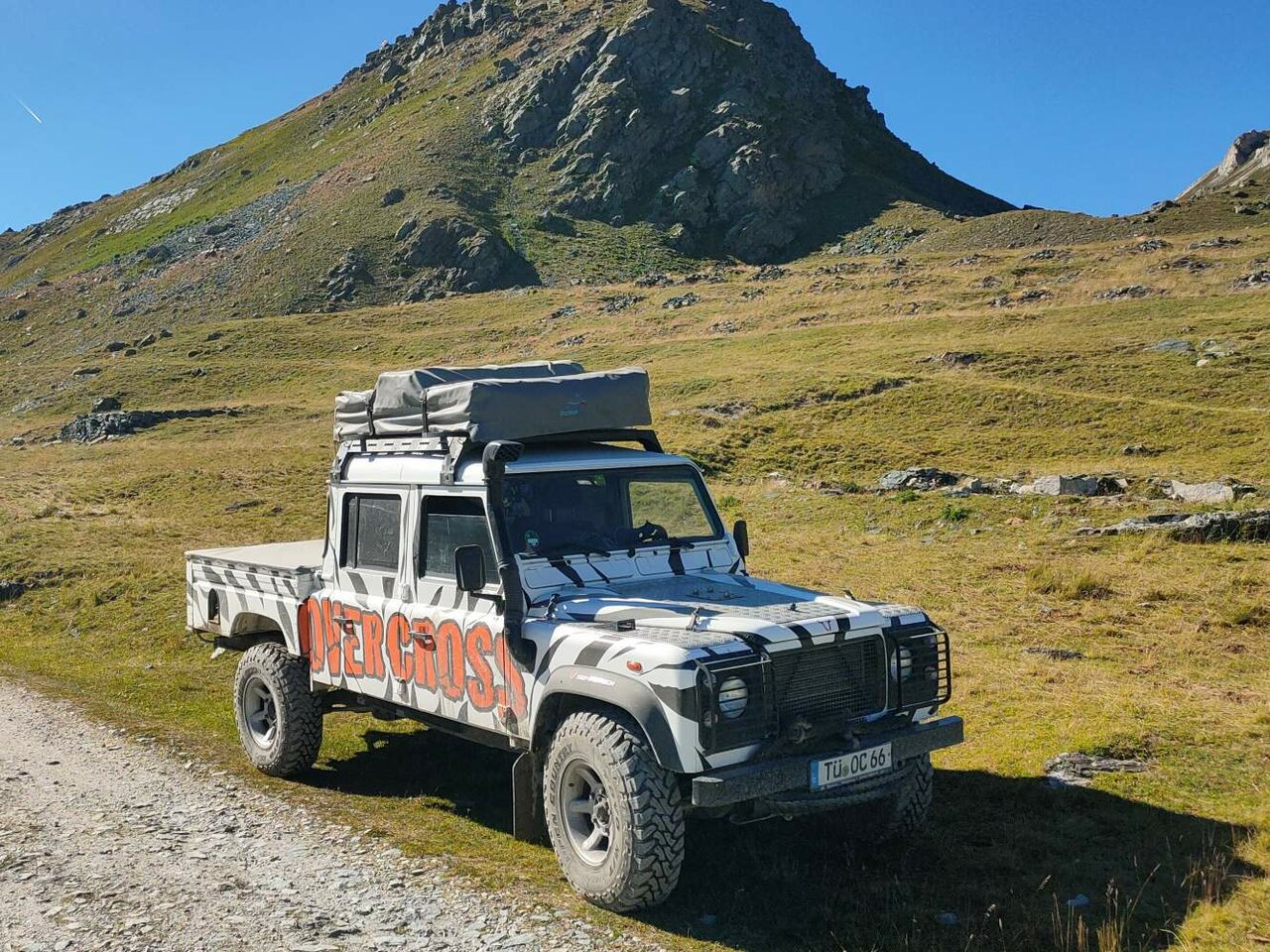 Ein Geländewagen mit Dachzelt steht auf einer Schotterpiste vor einem felsigen Gipfel