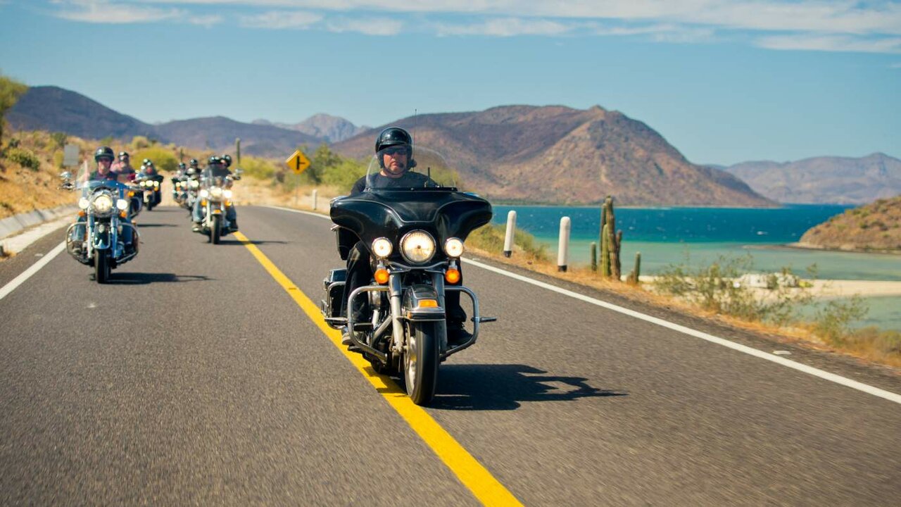 Harley-Davidson-Fahrer reihen sich auf einer Küstenstraße in Baja California, Kakteen und Hügel am Straßenrand