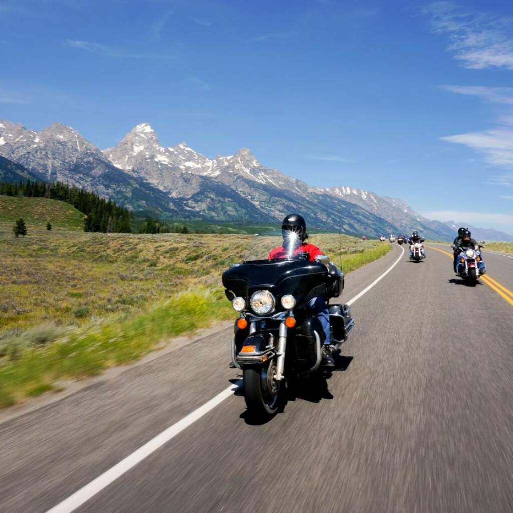 Motoristas en motos de viaje recorren una autopista bajo picos escarpados y nevados