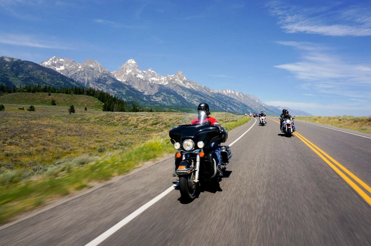 Motoristas en motos de viaje recorren una autopista bajo picos escarpados y nevados