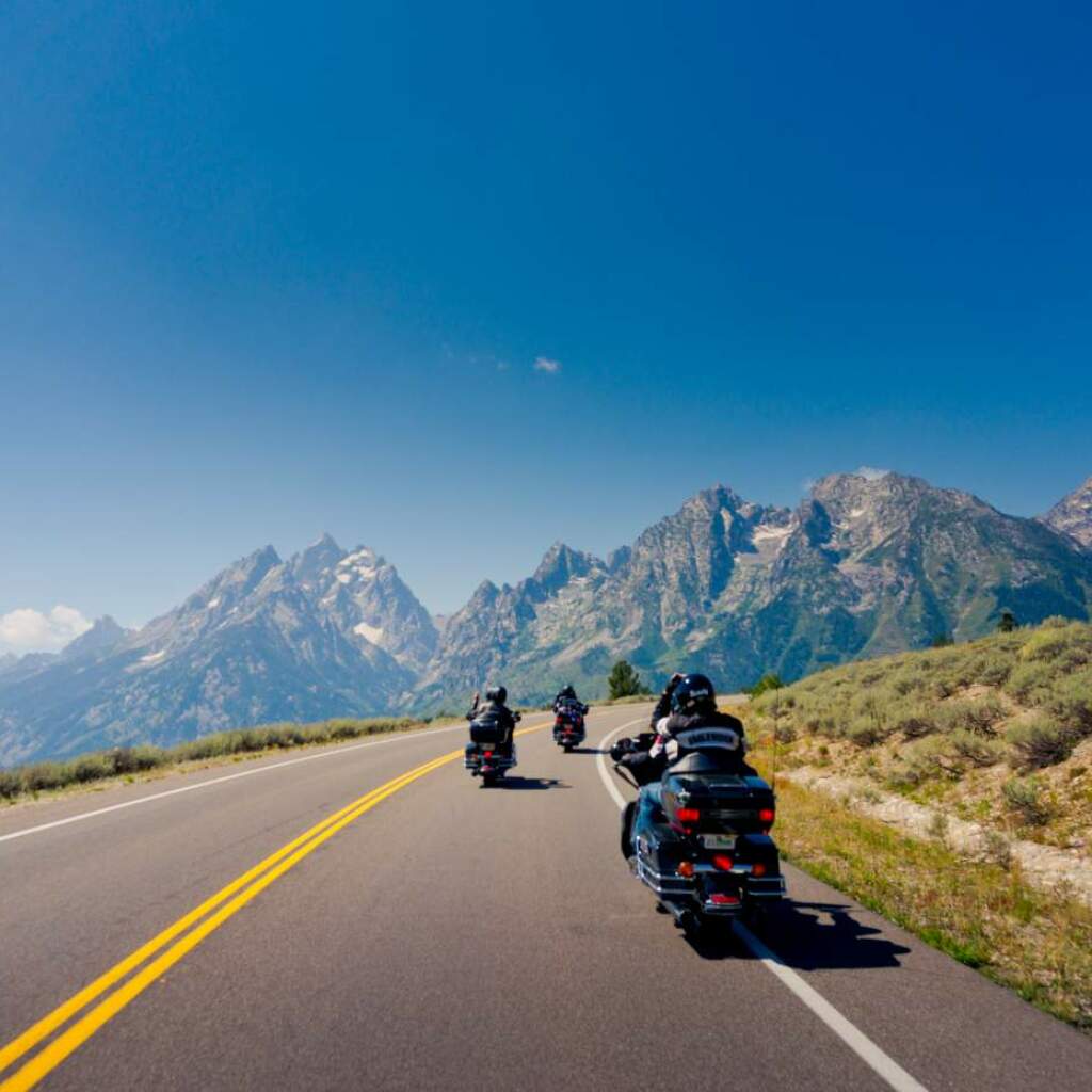 Motoristas se alejan de la cámara por una carretera con picos escarpados al frente