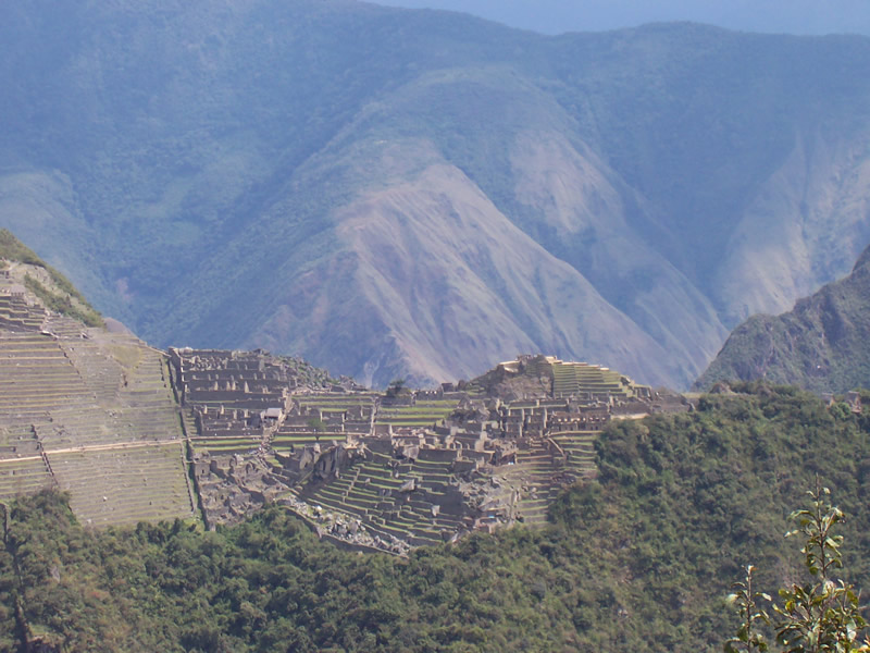 Machu Picchus terrassierte Steinruinen aus einem fernen, diesigen Blickwinkel, umgeben von bewaldeten Gipfeln