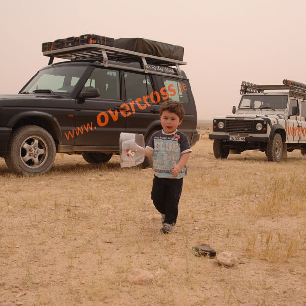 Ein kleines Kind geht durch die Wüste vor zwei geparkten overcross-4x4