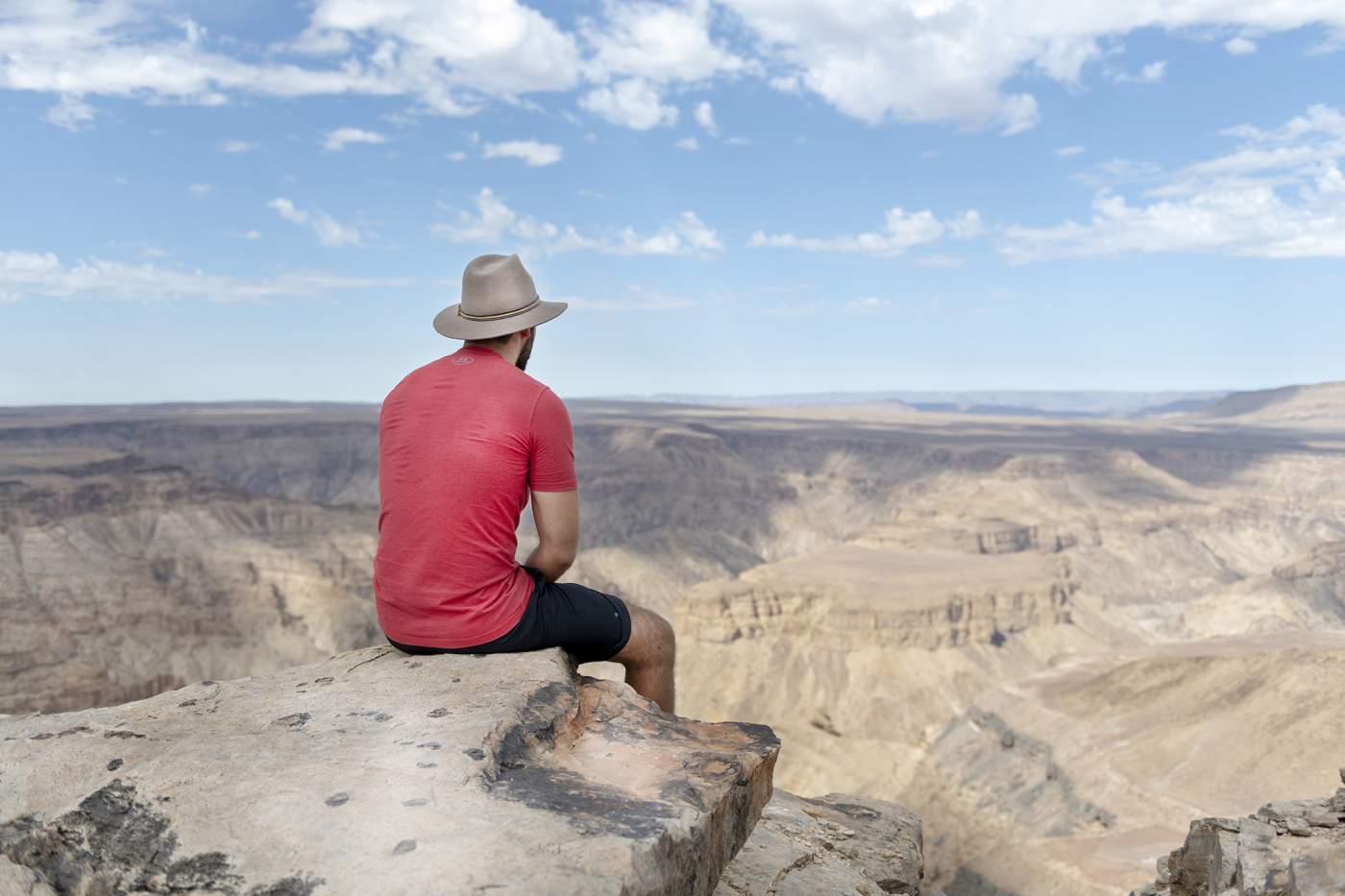 Mann sitzt auf einem Fels im Fish River Canyon in Namibia und bestaunt die überwältigende Landschaft.