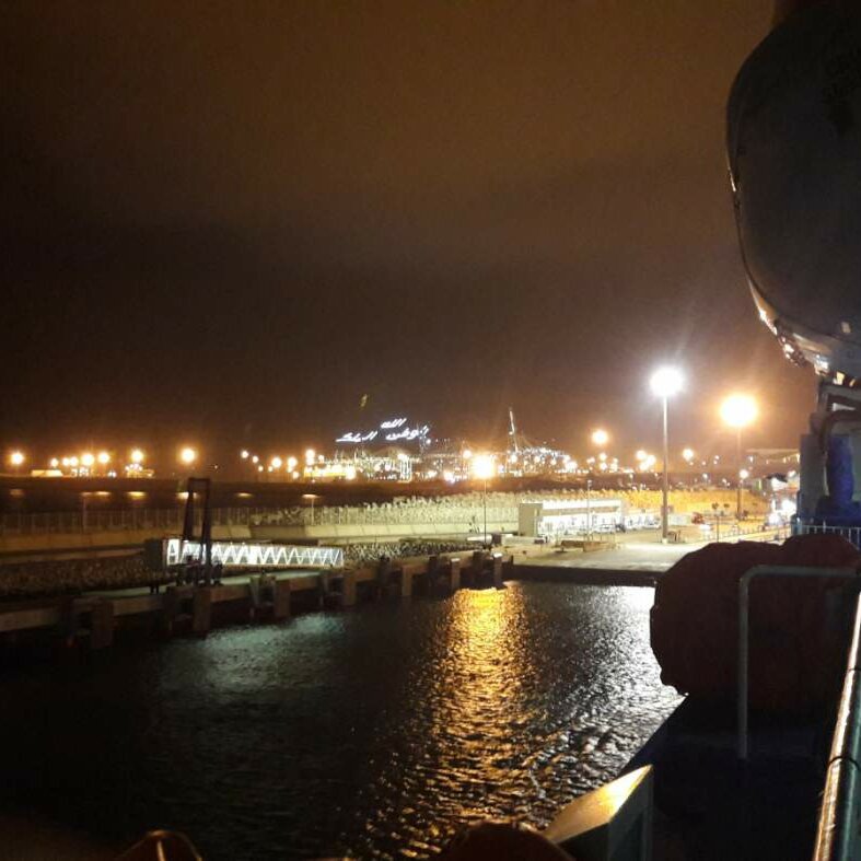 Ein Fährdeck bei Nacht mit Blick auf Hafenlichter und eine ferne Küste