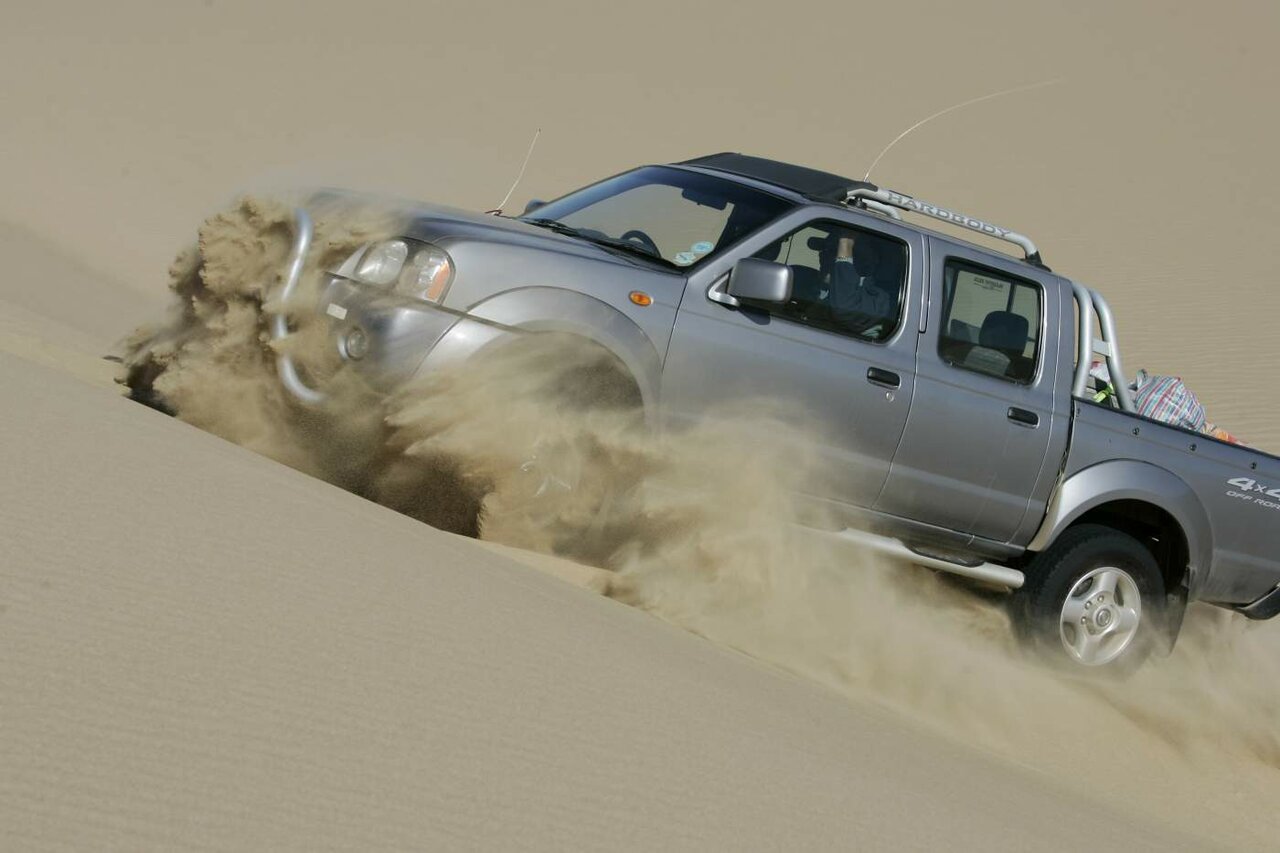 Ein 4x4-Pickup wirbelt beim Abfahren von einer Düne Sand auf