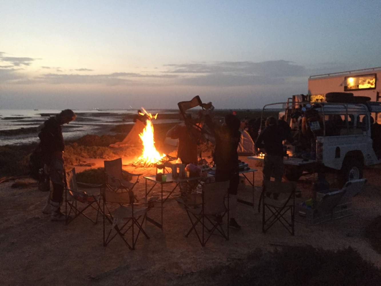 Enduro Camp mit Lagerfeuer am Strand bei Sonnenuntergang