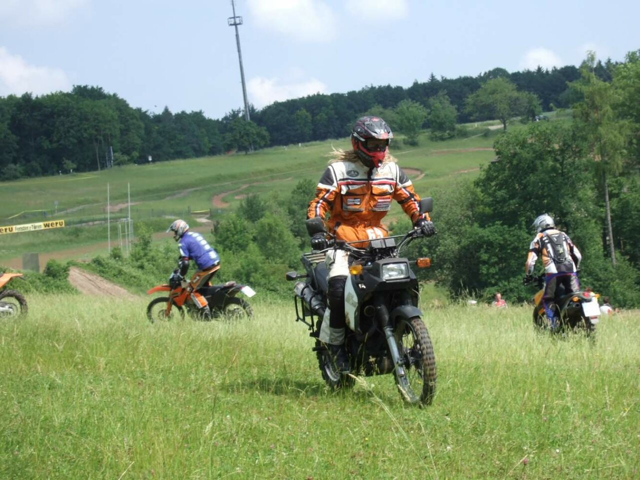 Eine Gruppe Enduro-Fahrer durchquert eine grüne Wiese beim Off-Road-Motorradtraining
