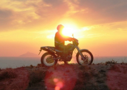 Silhouette eines Fahrers auf einem Motorrad bei Sonnenuntergang über dem Meer auf Kreta