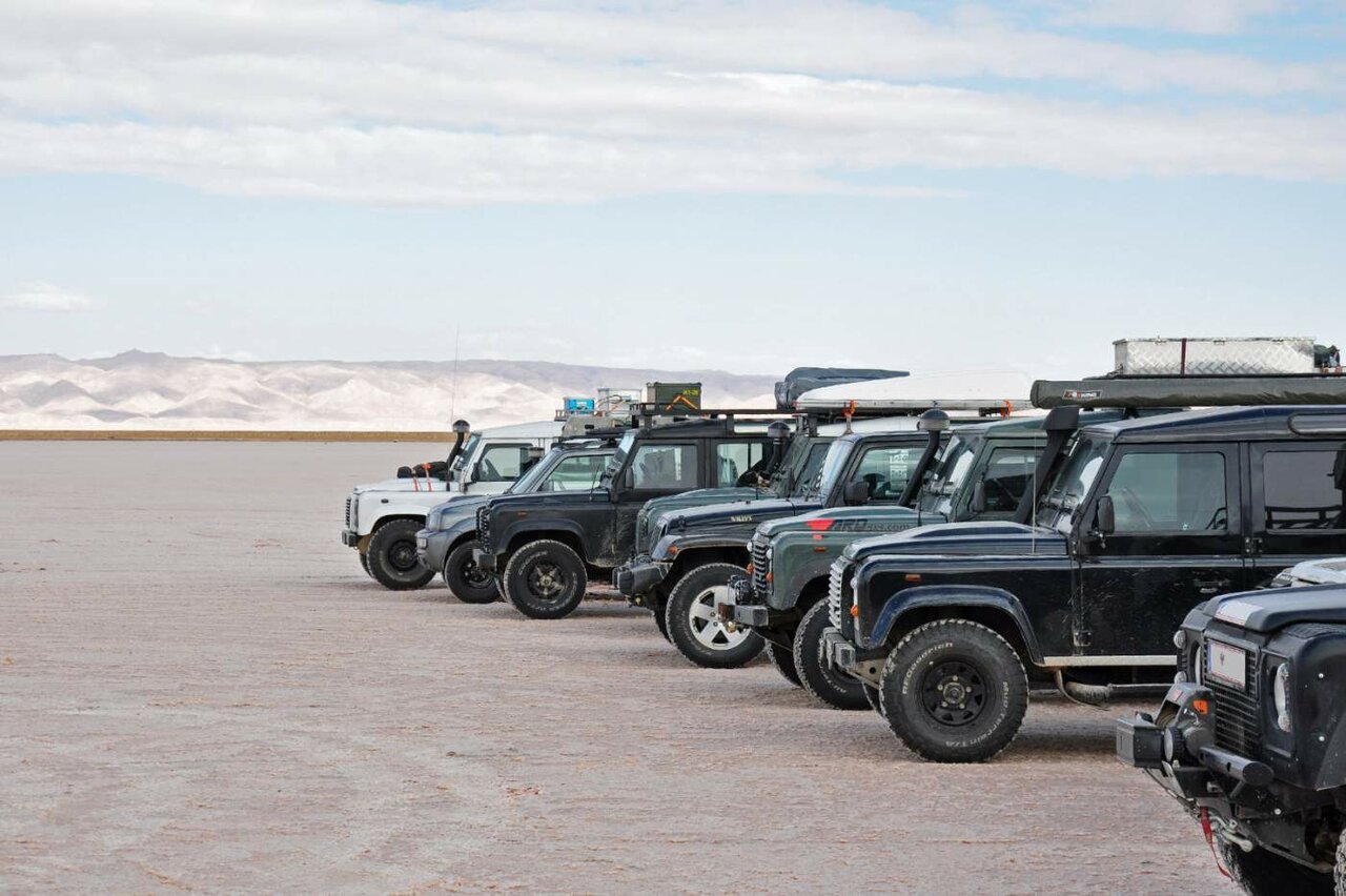 Several 4x4 off-road vehicles lined up on a pale desert plain with hazy mountains in the distance
