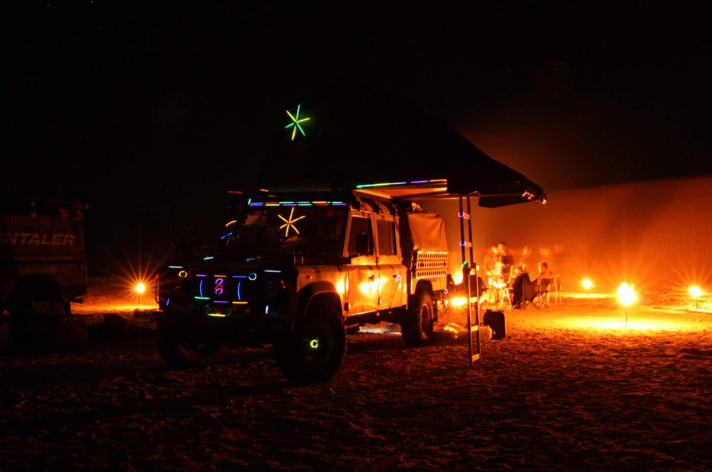 Mit Knicklichtern geschmückter Geländewagen als Weihnachtsbaum am Lagerfeuer