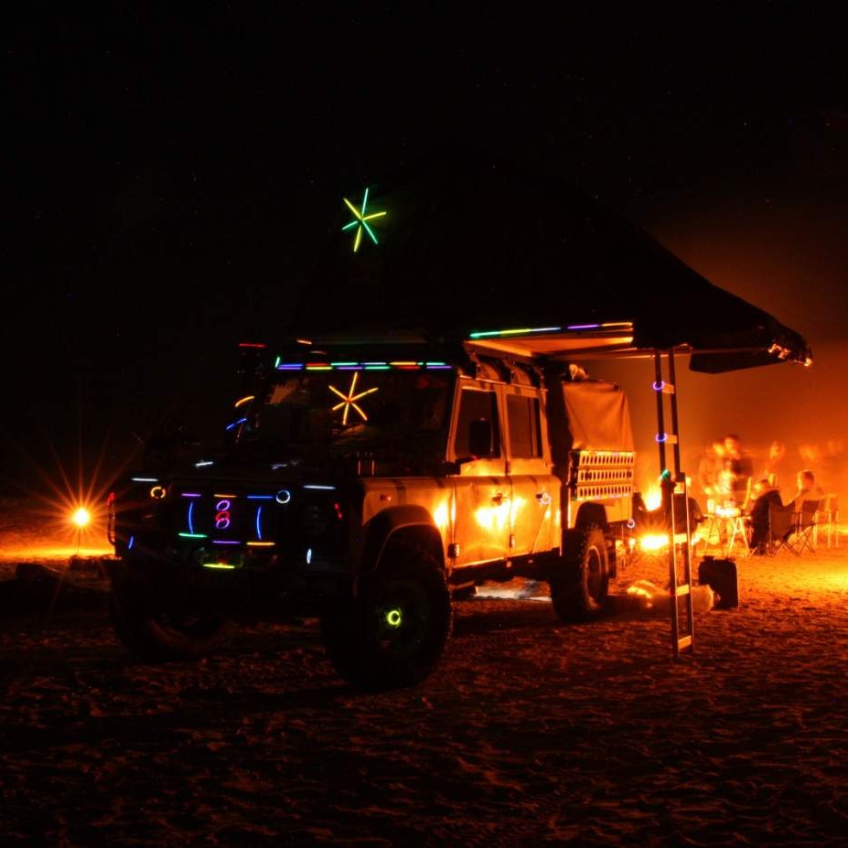 Mit Knicklichtern geschmückter Geländewagen als Weihnachtsbaum am Lagerfeuer