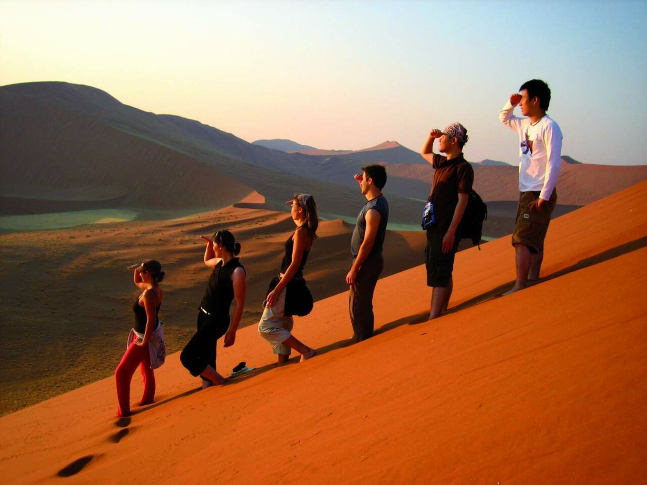 Eine Gruppe Wanderer geht bei Sonnenuntergang über einen Sanddünenkamm
