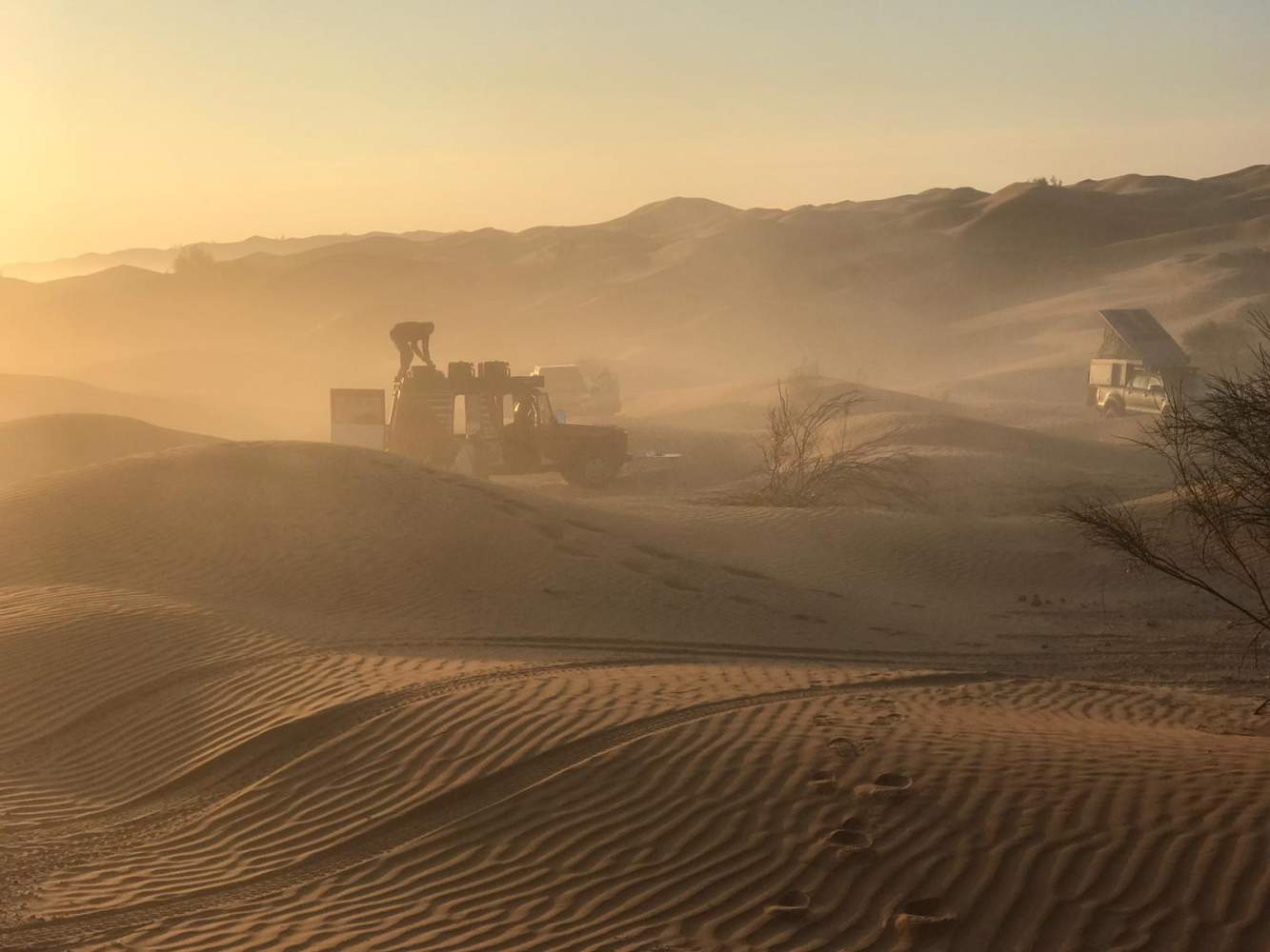 Aufbau des Camps nahe der Oase Ksar Ghilane während eines Sandsturms bei Sonnenuntergang