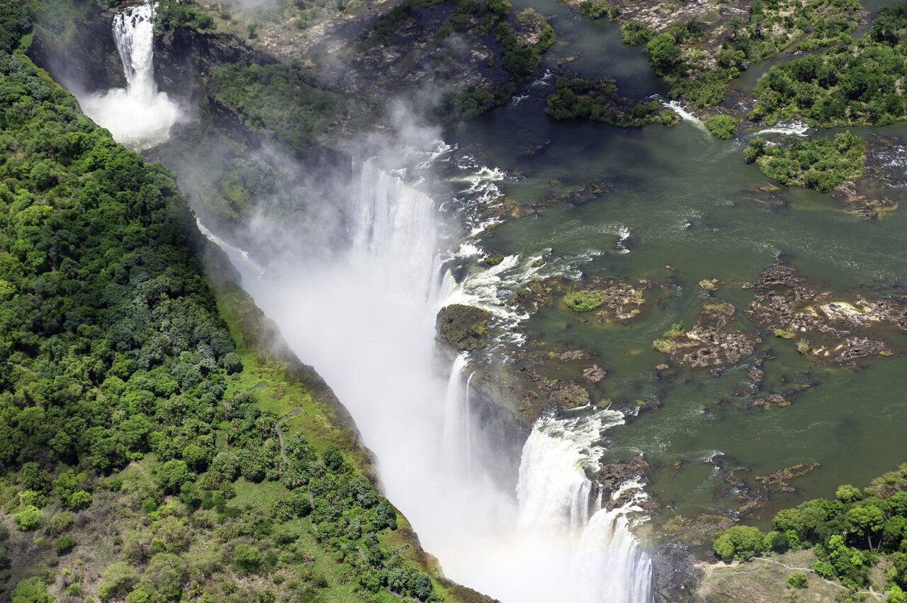 Vista aérea de uma ampla cachoeira caindo em um desfiladeiro com névoa, floresta em ambas as margens